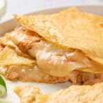 A close-up of a cheesy quesadilla on a white plate, served with lime wedges.