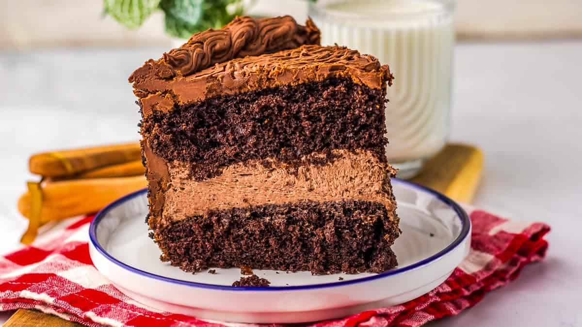 A slice of chocolate cake with multiple layers, including a creamy middle layer, topped with chocolate frosting.