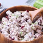 A wooden bowl filled with cranberry chicken salad with a wooden spoon.