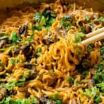 A pan of ramen noodles with mushrooms, greens, and a creamy sauce, served with chopsticks.