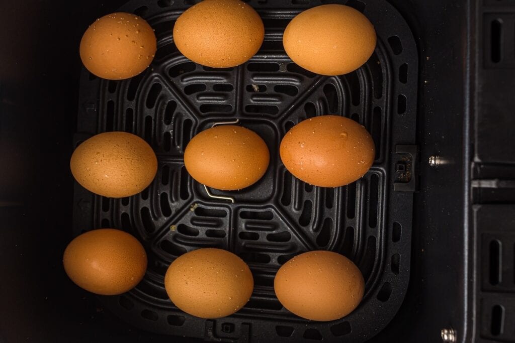 Nine brown eggs arranged in an air fryer basket.