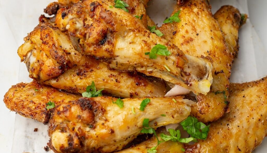 A pile of seasoned and cooked chicken wings garnished with chopped herbs on a white plate.