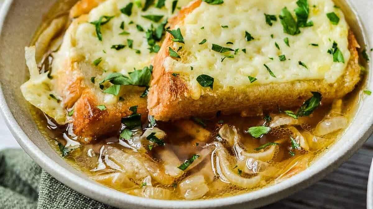 A bowl of French onion soup topped with melted cheese and chopped parsley on toasted bread, with a spoon in the bowl.