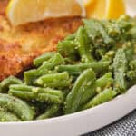 A plate with breaded chicken cutlet, roasted green beans with seasoning, and lemon wedges.