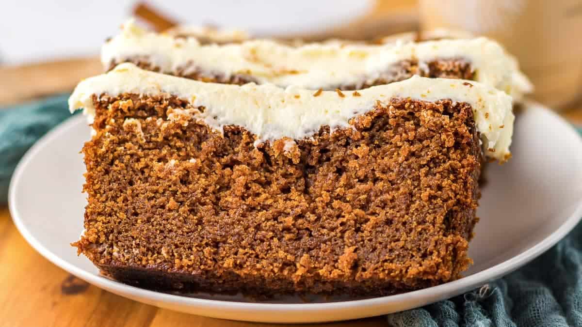 Two slices of gingerbread cake with cream cheese frosting on a white plate.