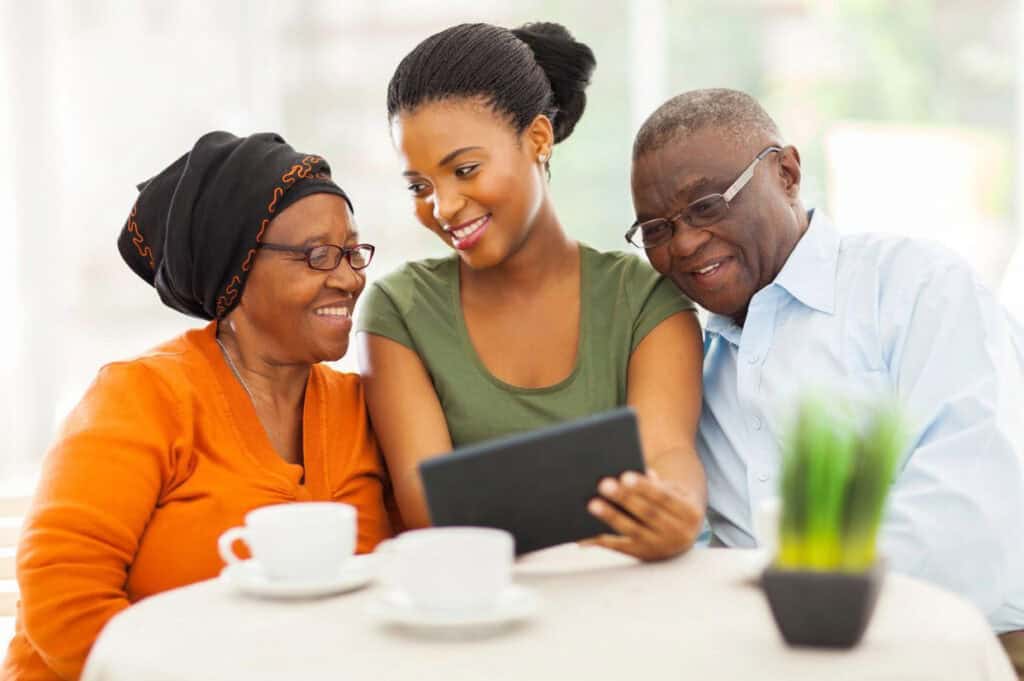 Three people sit at a table, smiling and looking at a tablet.