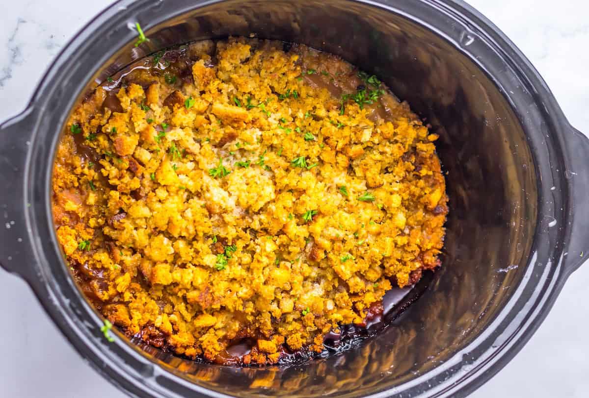 A slow cooker with a baked dish topped with golden brown, crumbly stuffing.