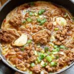 Skillet with noodle soup, ground meat, sliced garlic, and chopped green onions.