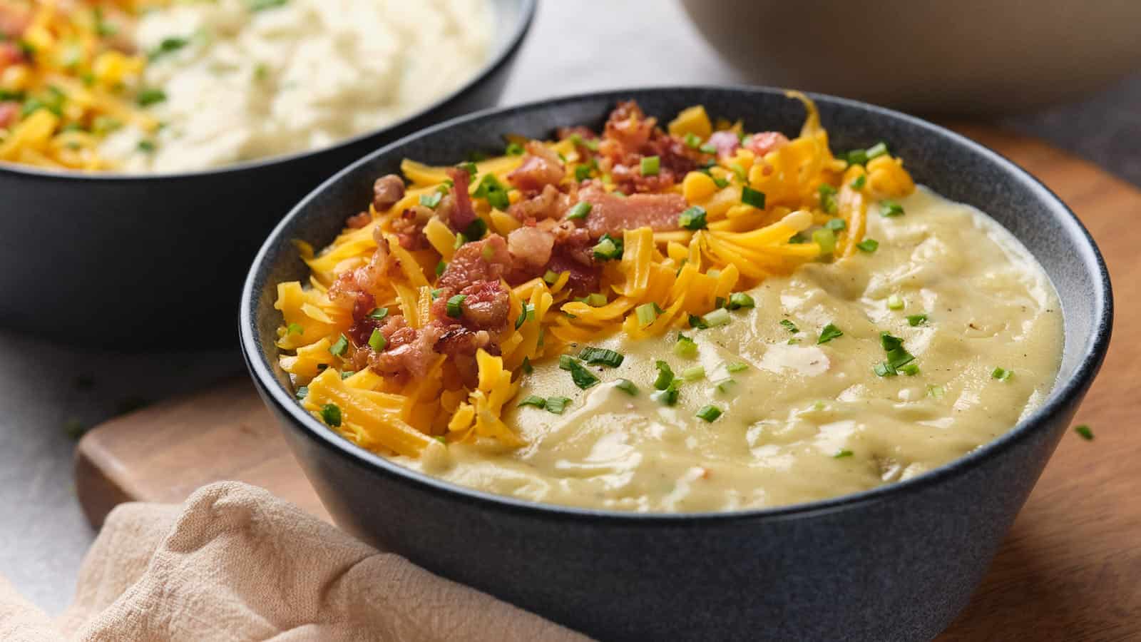 A bowl of outback potato soup topped sits on a wooden surface.