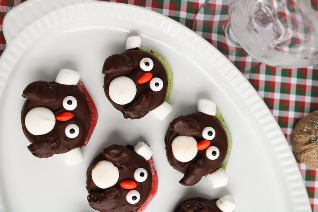 Chocolate penguin cookies with marshmallow accents on a white plate, set on a plaid tablecloth.