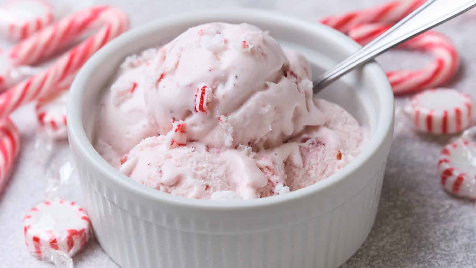 A bowl of peppermint ice cream with a spoon, surrounded by candy canes and peppermint candies.