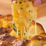 A piece of cheesy garlic bread being pulled apart, showing melted cheese and herbs.