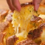 A hand pulls a piece from a cheesy garlic pull-apart bread, with melted cheese stretching.