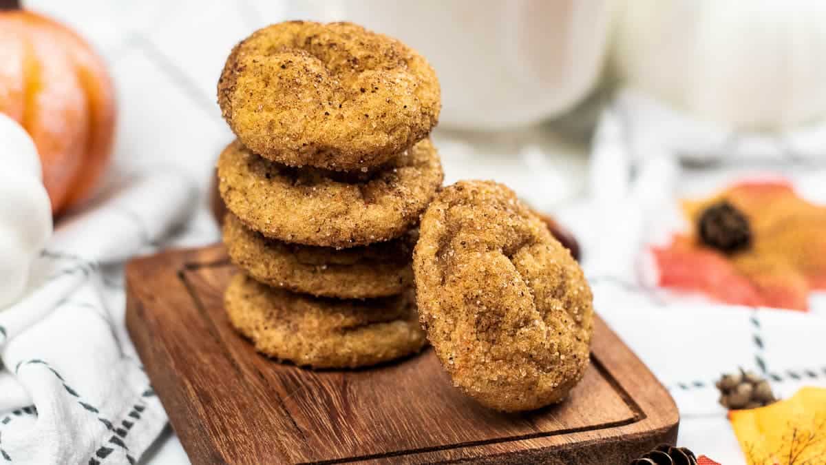 A stack of four pumpkin snickerdoodles sits on a wooden board.