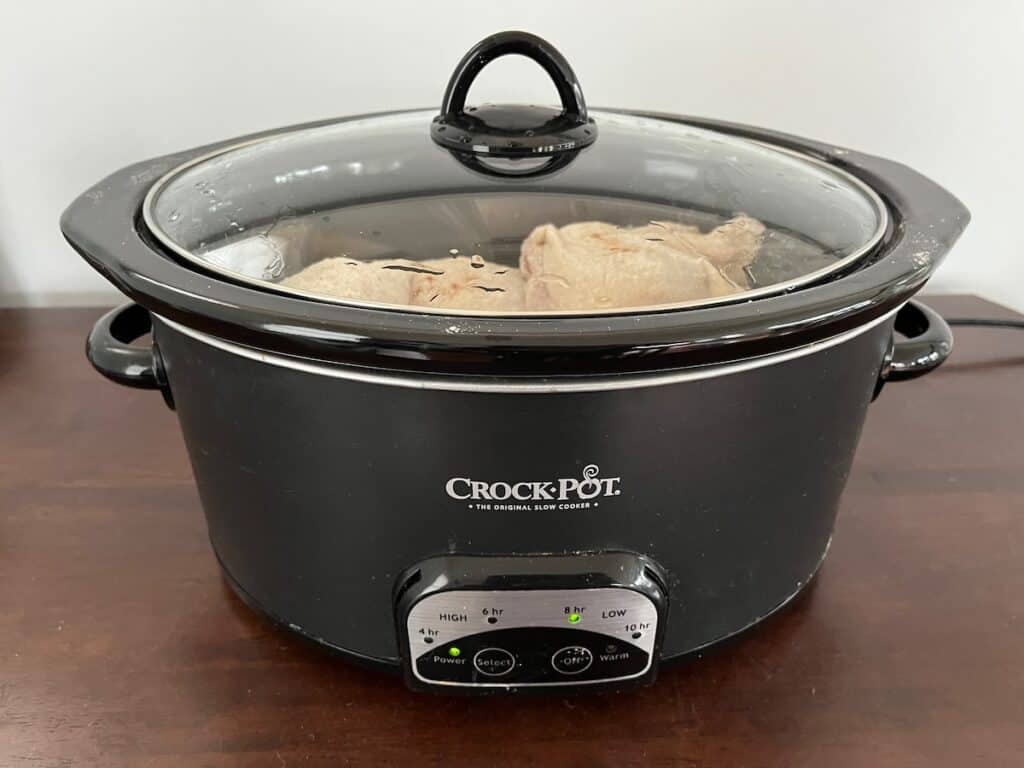 Black Crock-Pot slow cooker on a wooden table with lid closed, cooking food inside.