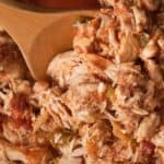 Close-up of shredded chicken mixed with diced tomatoes and green peppers, stirred with a wooden spoon.