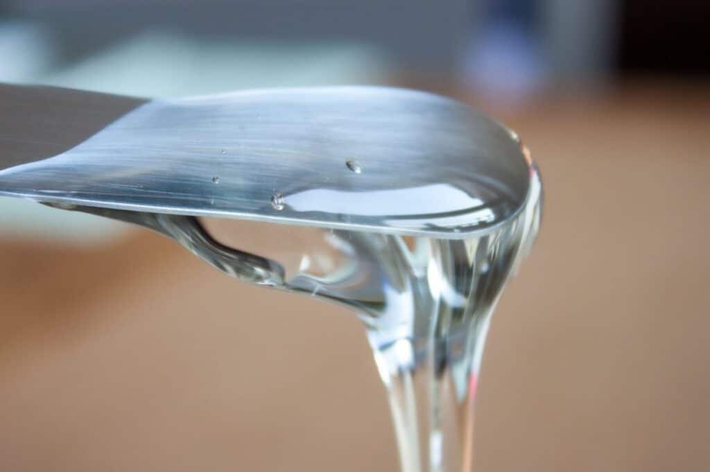 Close-up of a metal spatula with transparent gel-like substance dripping from its edge.