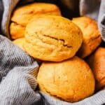 A close-up of round, golden-brown biscuits nestled in a gray, striped cloth.