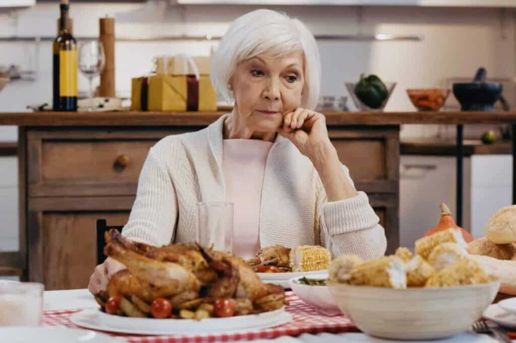 An elderly woman sits at a table looking upset on Thanksgiving.