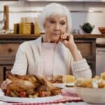 An elderly woman sits at a table looking upset on Thanksgiving.