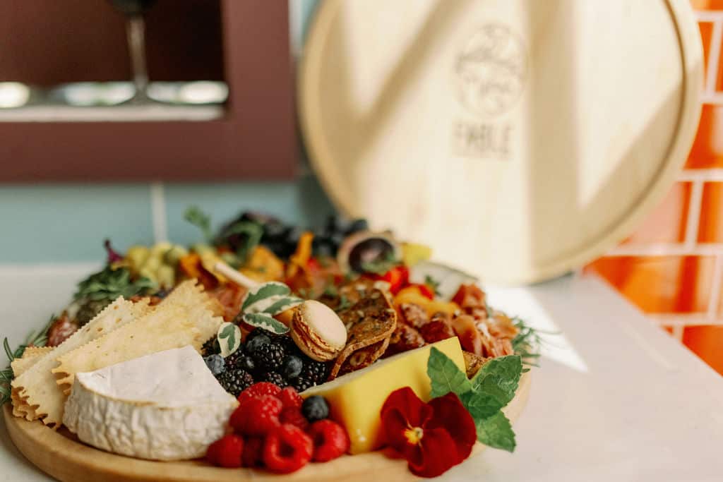 A wooden board with various cheeses, crackers, berries, nuts, and decorative flowers.