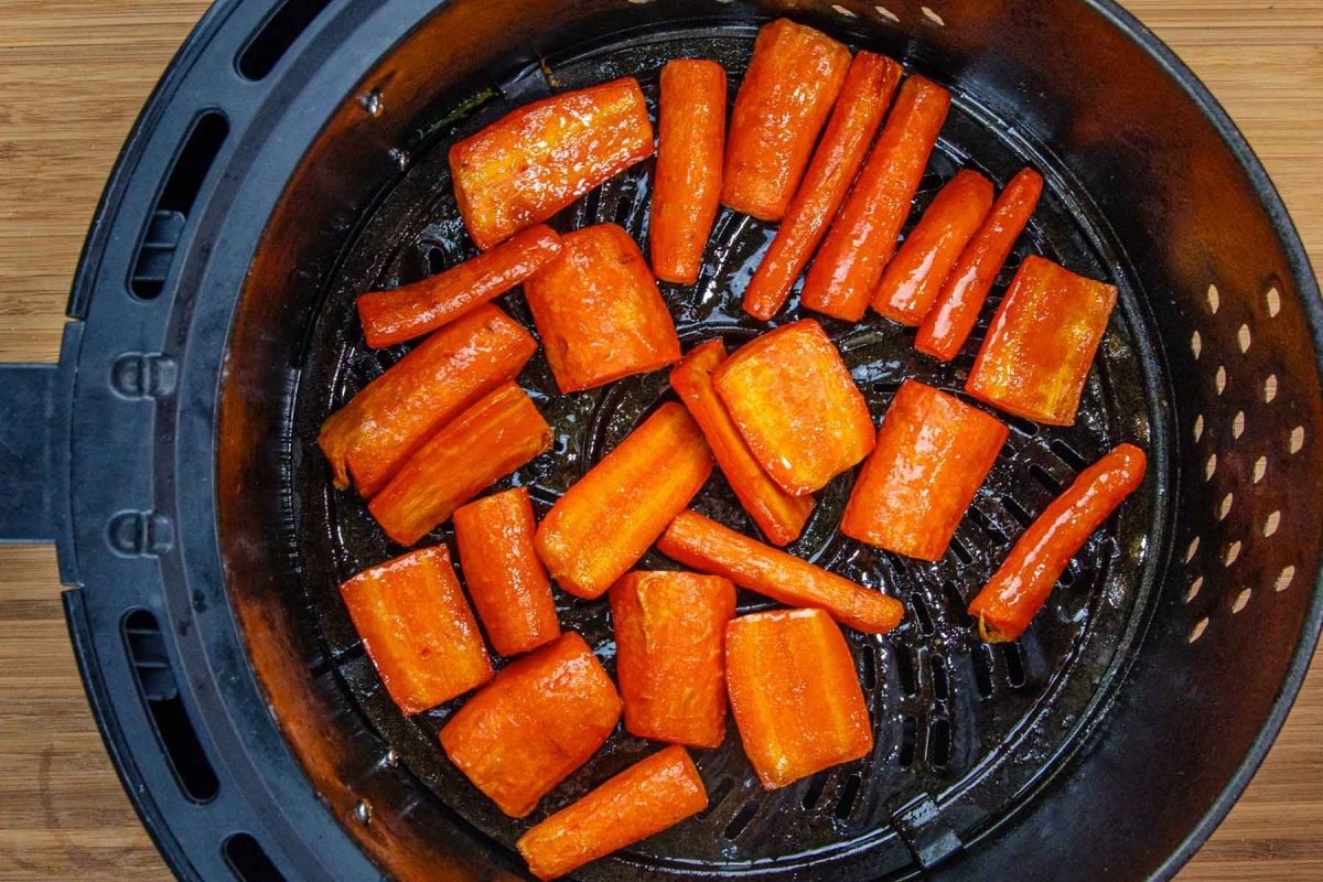 Diced and whole carrots in an air fryer basket on a wooden surface.