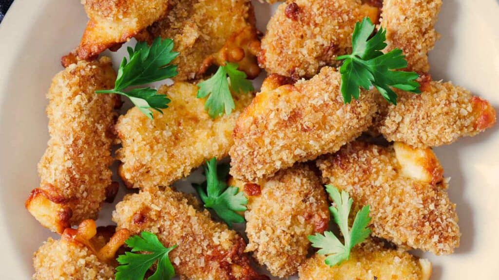 Close-up of crispy breaded chicken tenders garnished with fresh parsley on a plate.