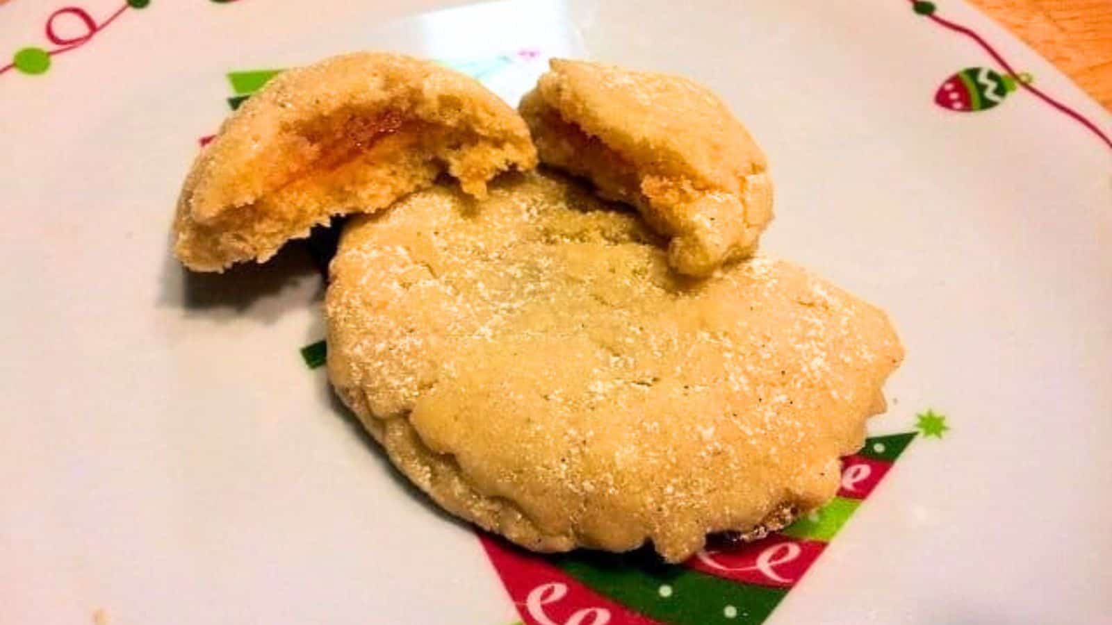 A sugar-dusted cookie with a bite revealing an orange filling, placed on a festive plate with holiday decorations.