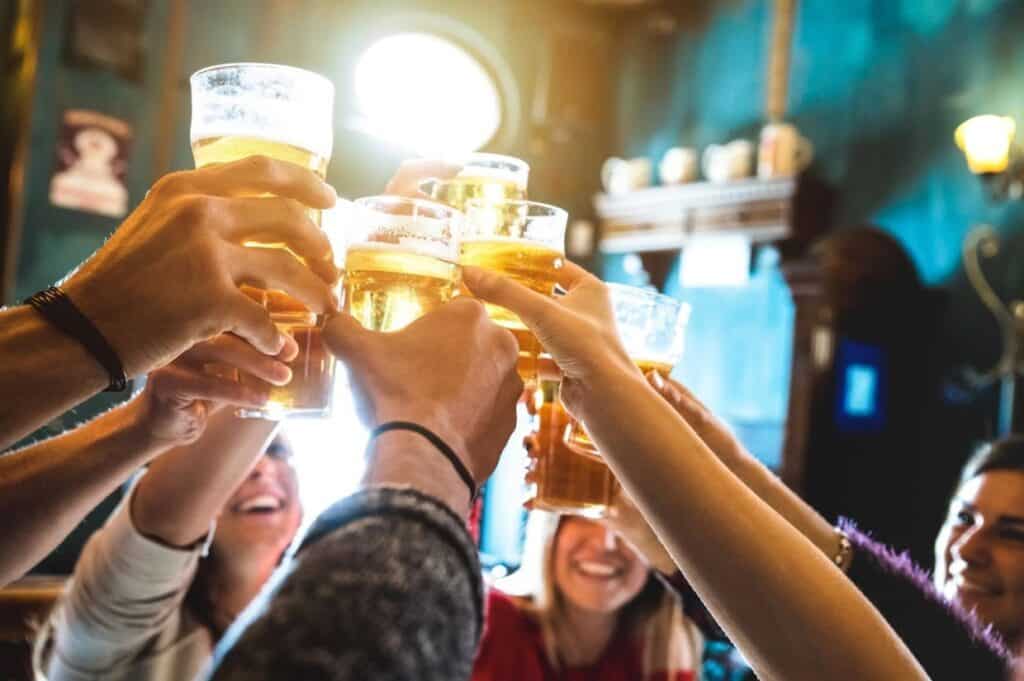 A group of people raise glasses of beer in a toast inside a dimly lit pub.