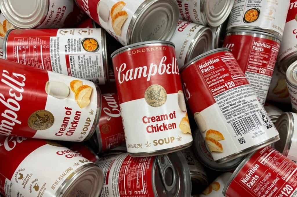 A pile of Campbell's Cream of Chicken soup cans, displaying labels with red and white design.