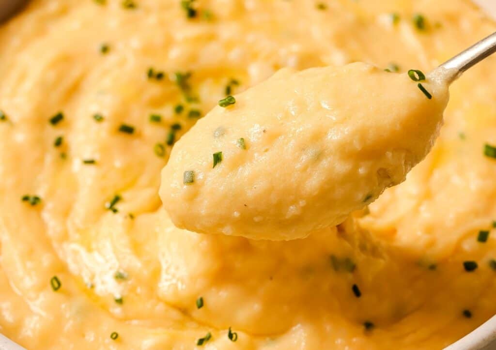 Close-up of a spoonful of creamy mashed potatoes garnished with chopped chives.