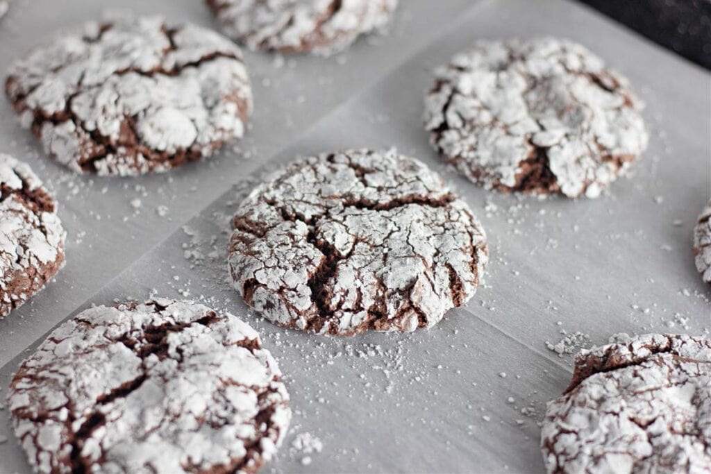 Chocolate crinkle cookies with powdered sugar on parchment paper.