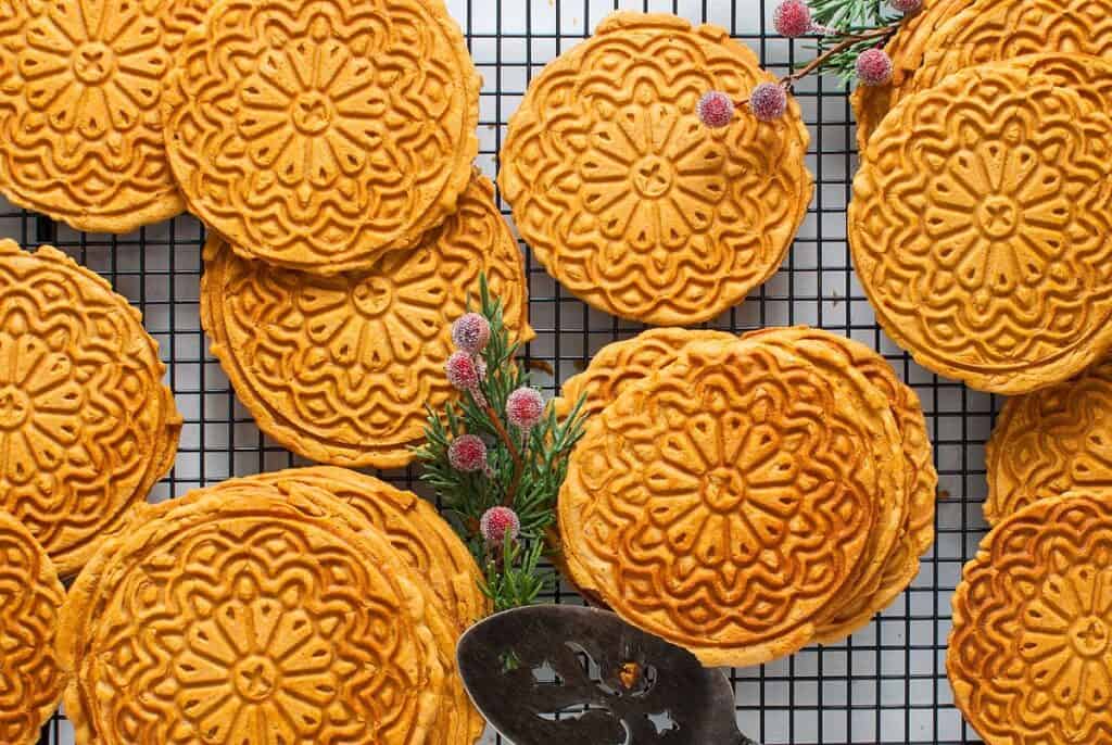 Golden, intricately patterned cookies are displayed on a cooling rack, with a decorative sprig and a metal spatula nearby.