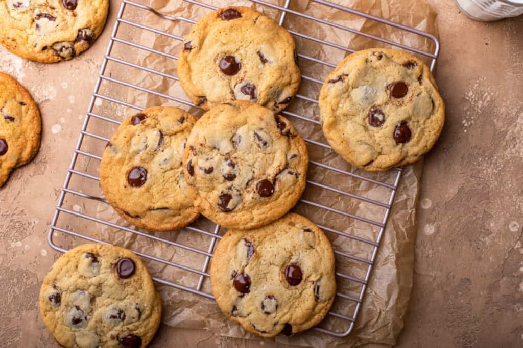 Freshly baked chocolate chip cookies cooling on a wire rack, placed on crumpled parchment paper.