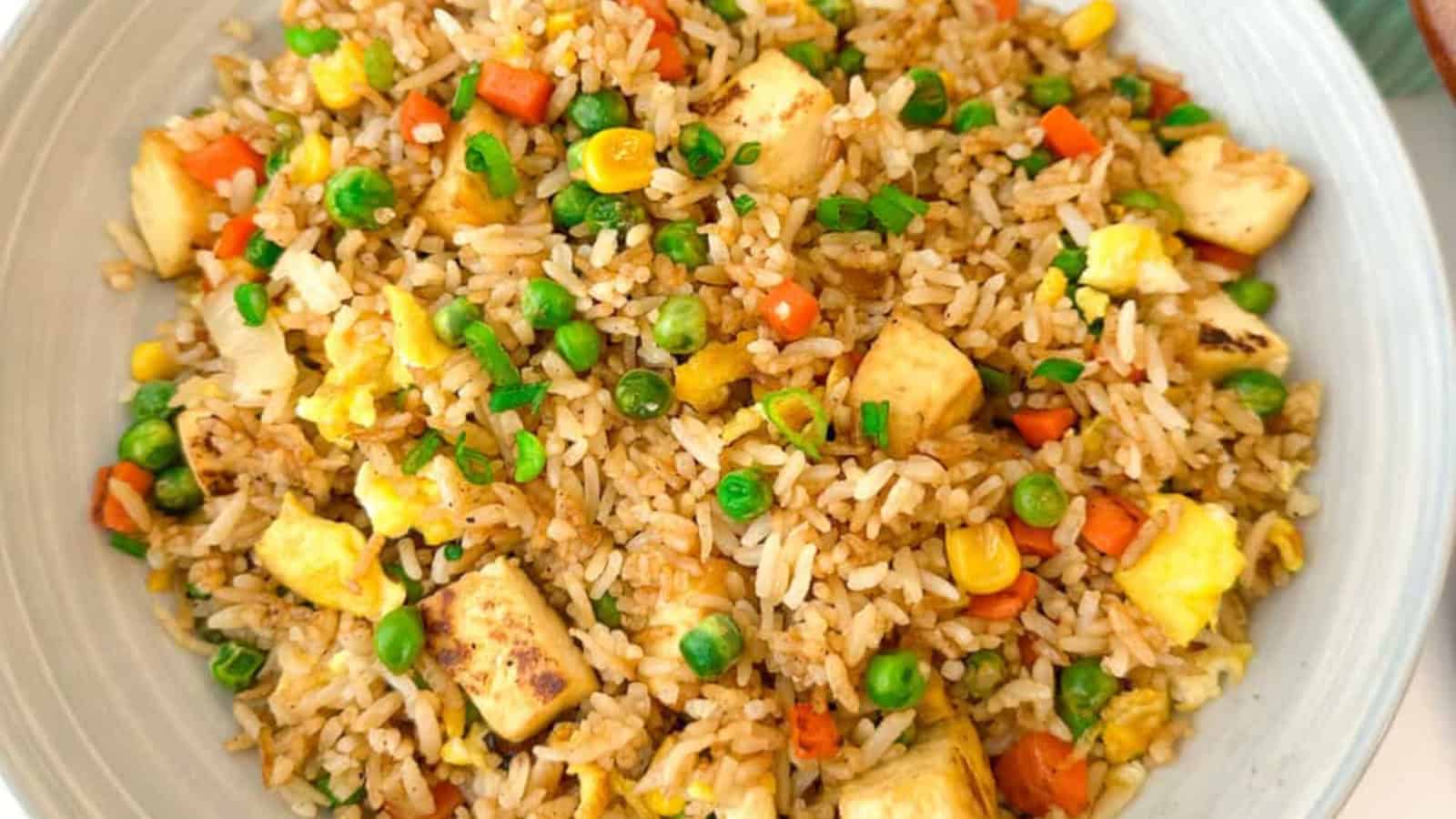 A plate of fried rice with tofu, peas, corn, carrots, and egg.