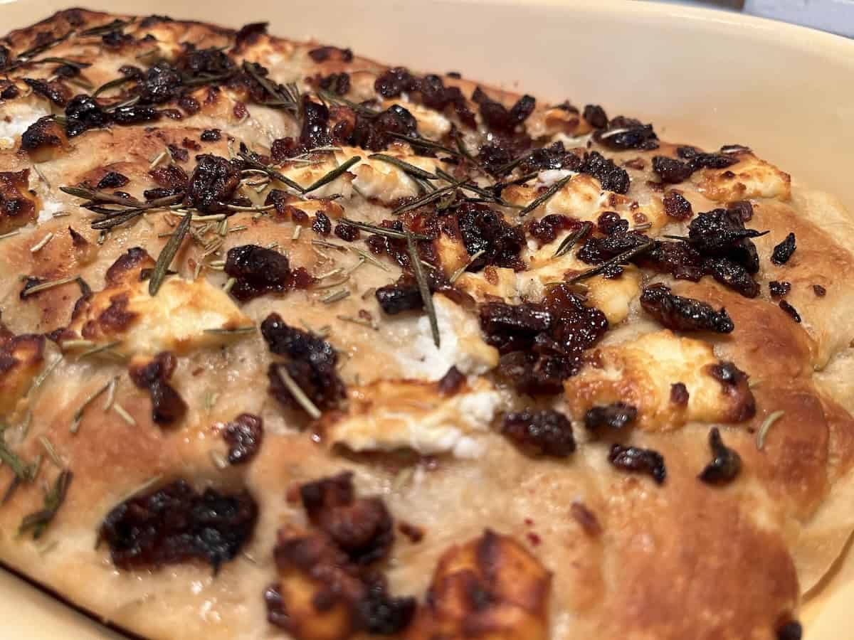 A close-up of freshly baked focaccia topped with rosemary, caramelized onions, and cheese.