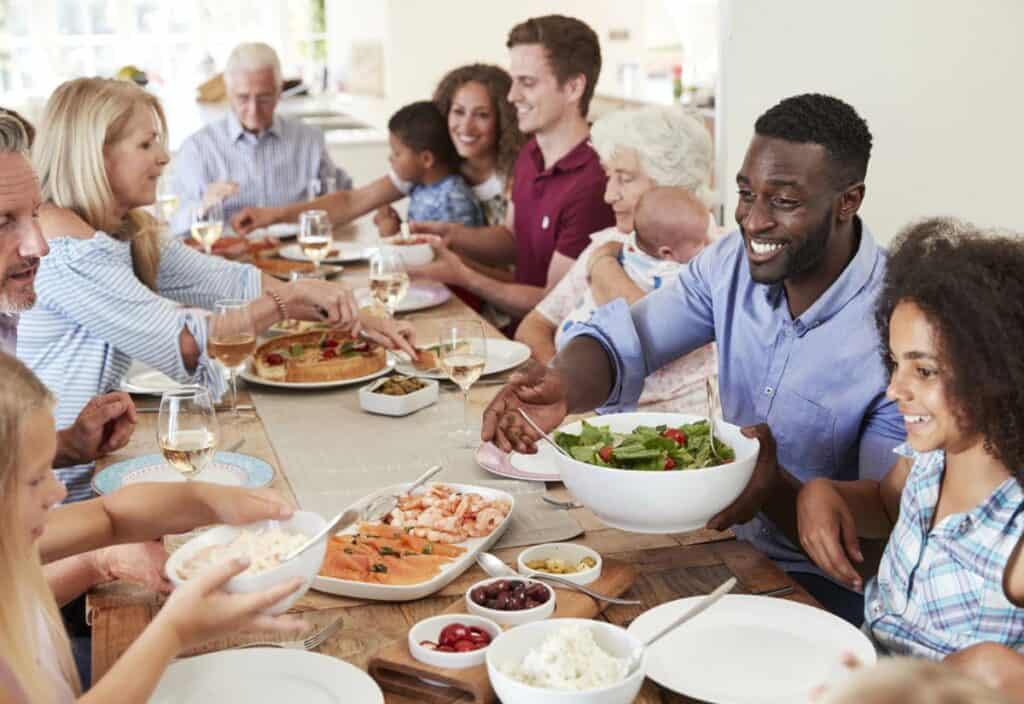 A diverse group of people enjoying a meal together at a long table, sharing dishes and talking.