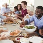 A diverse group of people enjoying a meal together at a long table, sharing dishes and talking.