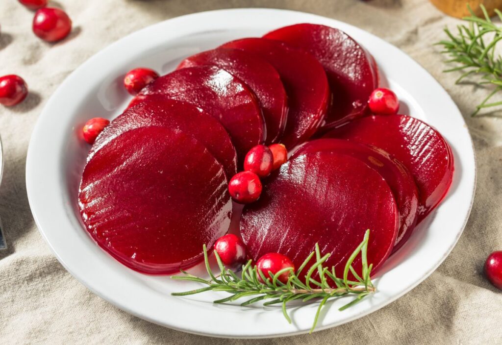 Sliced canned cranberry sauce on a white plate, garnished with whole cranberries and rosemary sprigs.