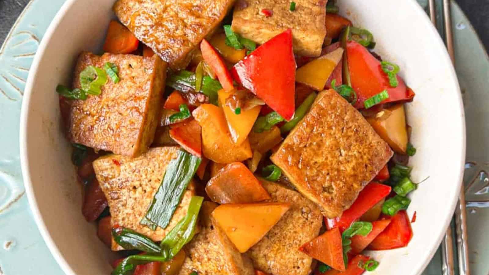 A bowl of stir-fried tofu with sliced red and orange bell peppers, topped with green onions.