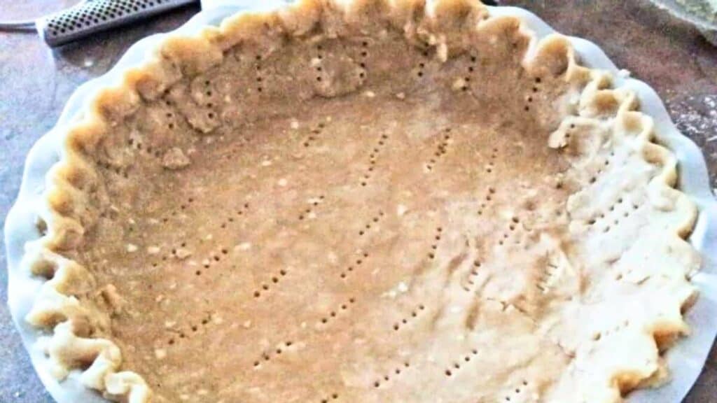 Unbaked pie crust in a fluted dish with fork holes for venting, placed on a countertop.