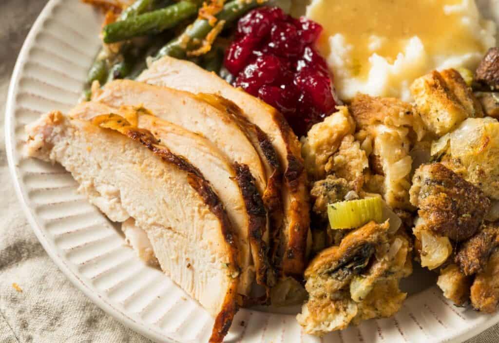 A plate with sliced turkey, reminiscent of tired turkey sandwiches, is paired with stuffing, green beans, mashed potatoes with gravy, and cranberry sauce.