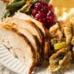 A plate with sliced turkey, reminiscent of tired turkey sandwiches, is paired with stuffing, green beans, mashed potatoes with gravy, and cranberry sauce.