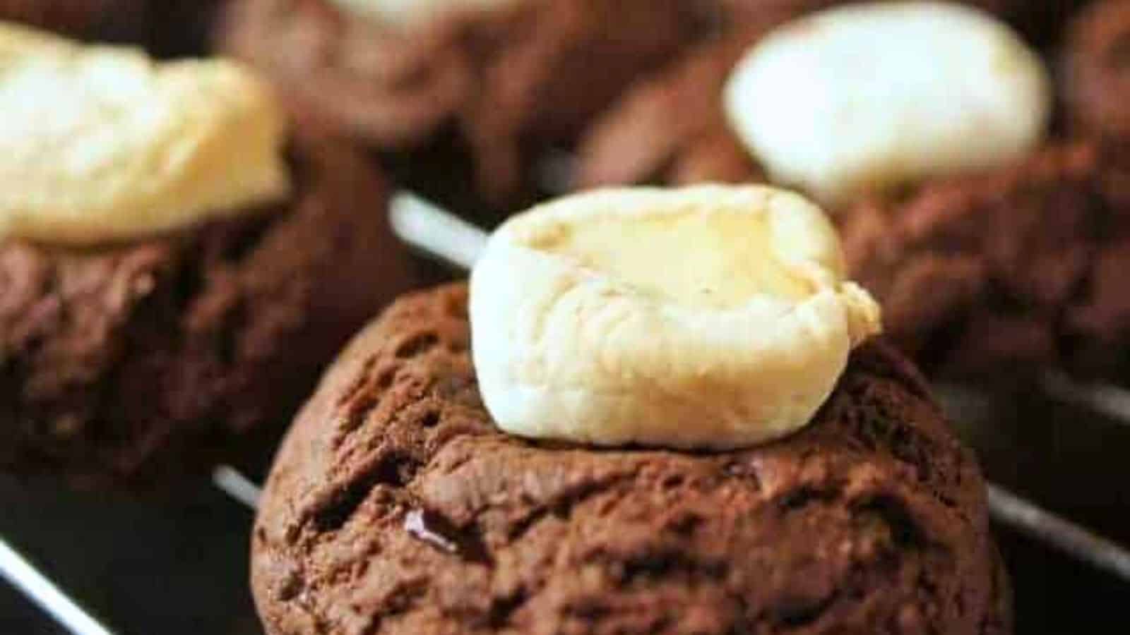 Close-up of chocolate cookies with marshmallow centers on a cooling rack.