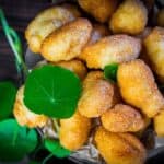 A basket filled with golden-brown, crispy fritters garnished with small green leaves on top.