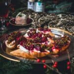 A festive platter with bruschetta topped with ricotta, cranberries, and herbs on a gold tray, surrounded by holiday decorations.