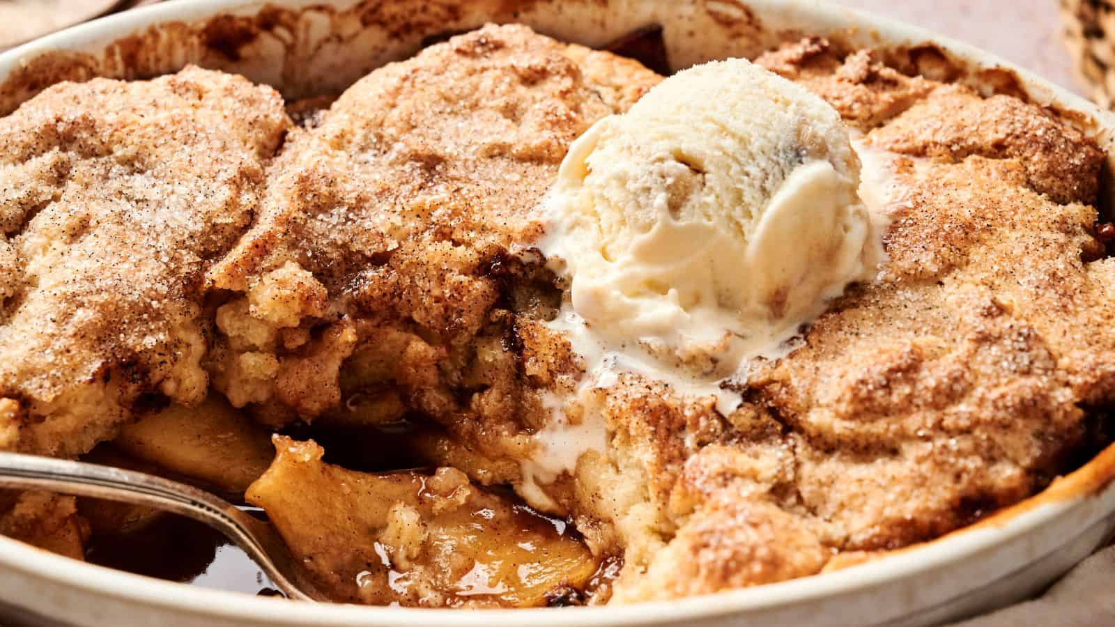 A baked apple cobbler with a scoop of vanilla ice cream on top, partially served in a dish.