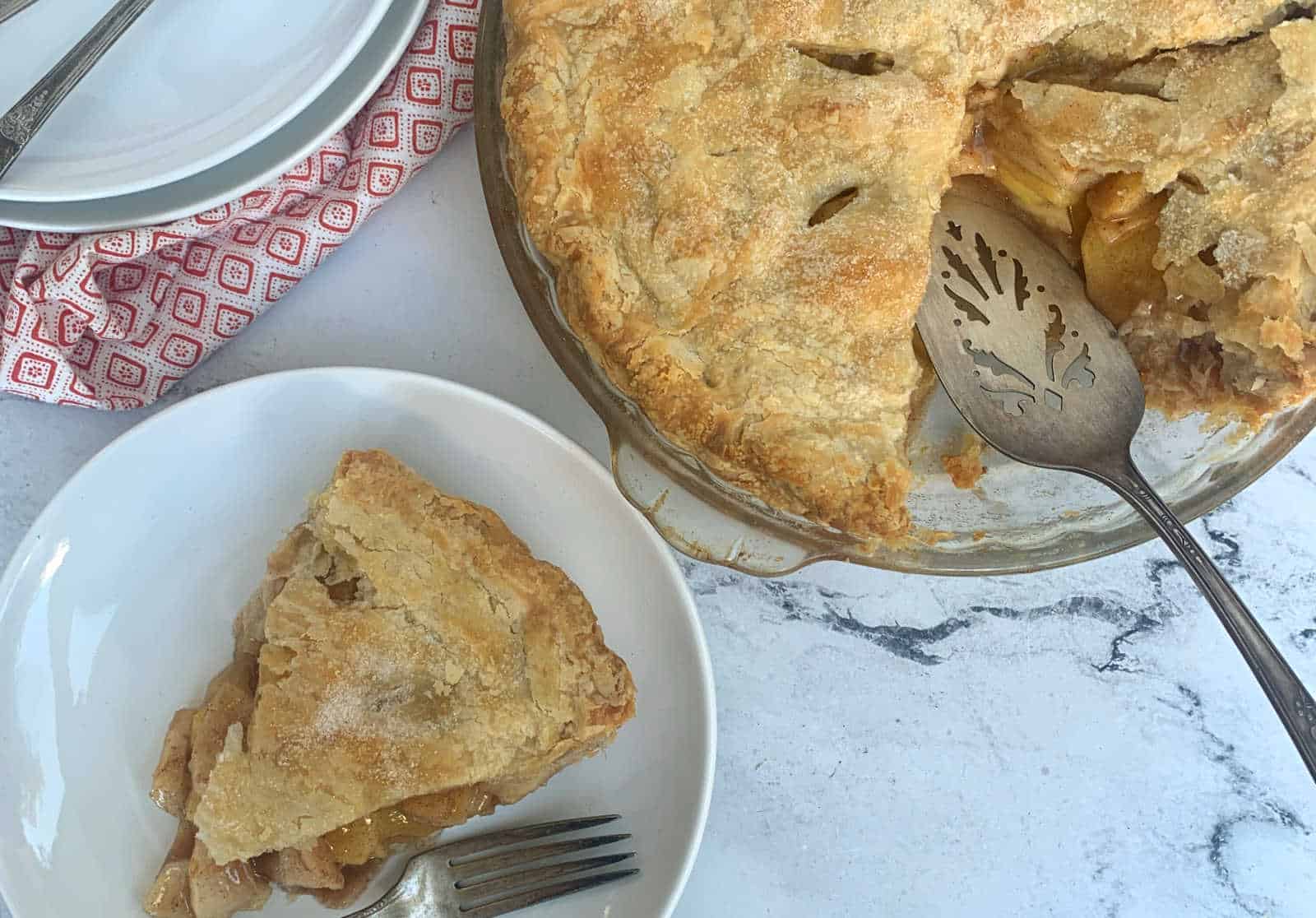 Apple pie with a lattice crust on a marble surface, one slice on a