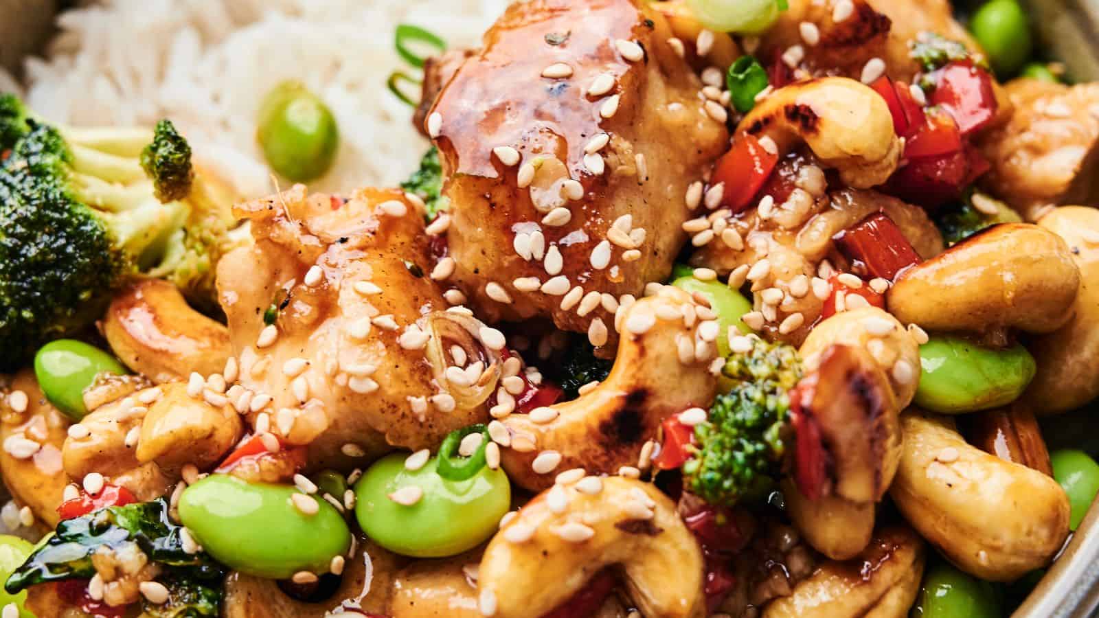 Close-up of Cashew Chicken featuring tender chicken, broccoli, edamame, cashews, and red bell peppers. This delicious dish is topped with sesame seeds and served over a bed of rice.