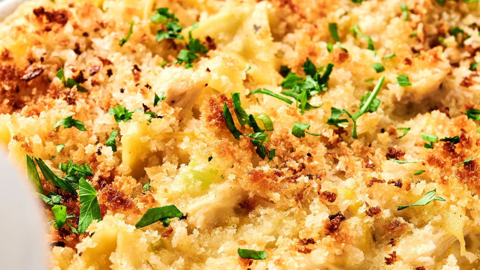 Close-up of a chicken noodle casserole with a golden breadcrumb topping, garnished with chopped herbs.